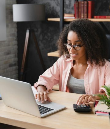 Freelancer counting funds domestic bills on calculator using laptop for e-banking,debt and loan